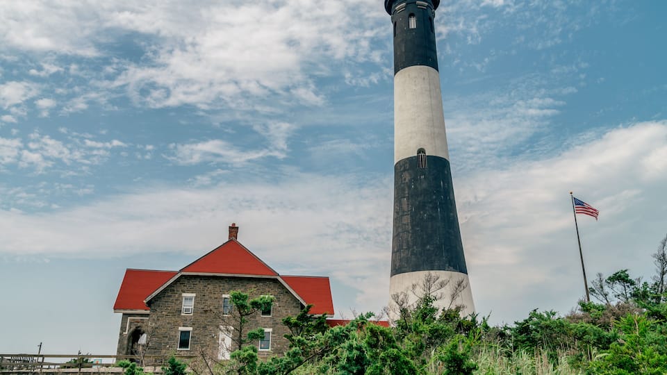 A lighthouse with a red roof and a stone building nearby.