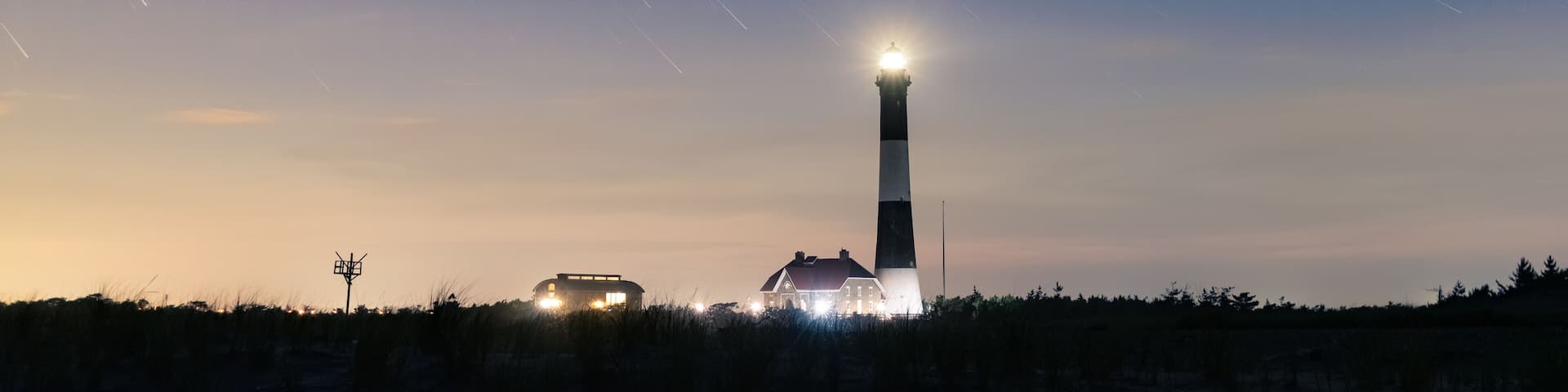 Star trails over a tall lighthouse on the coast. Fire Island National Seashore, Long Island New York.
