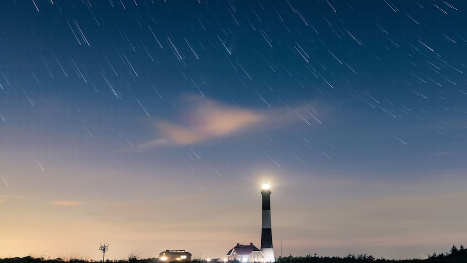 A lighthouse at dusk with star trails in the sky.