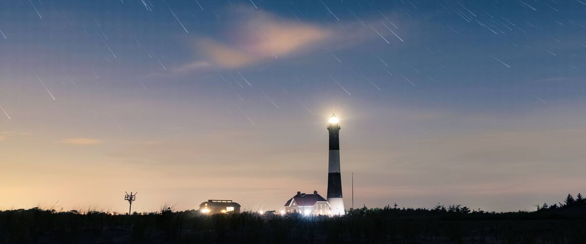 Star trails over a tall lighthouse on the coast. Fire Island National Seashore, Long Island New York.
