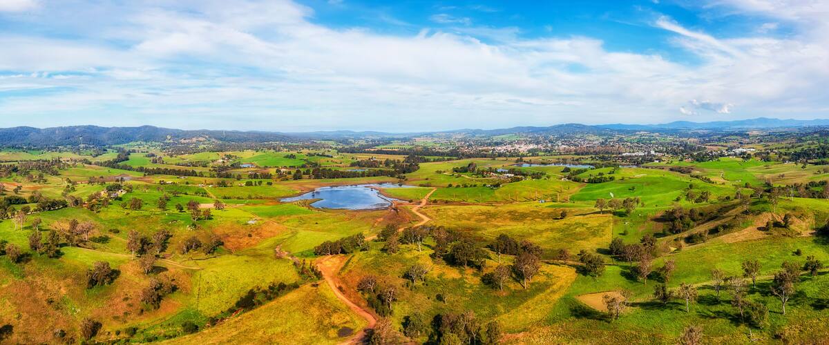 A panoramic view of a lush green valley with rolling hills, a small lake, and distant mountains under a clear sky.