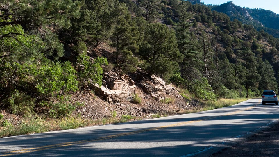 A car passes a pinyon-juniper forest at dawn in Cimarron Canyon State Park in the Sangre de Cristo Range of the Rocky Mountains