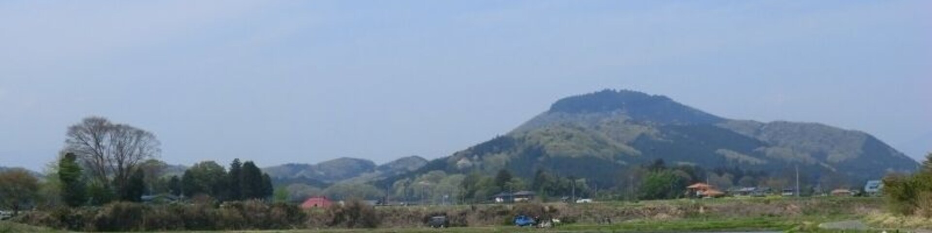 Paisagem rural com estrada, plantações de arroz e uma colina ao fundo com casas.