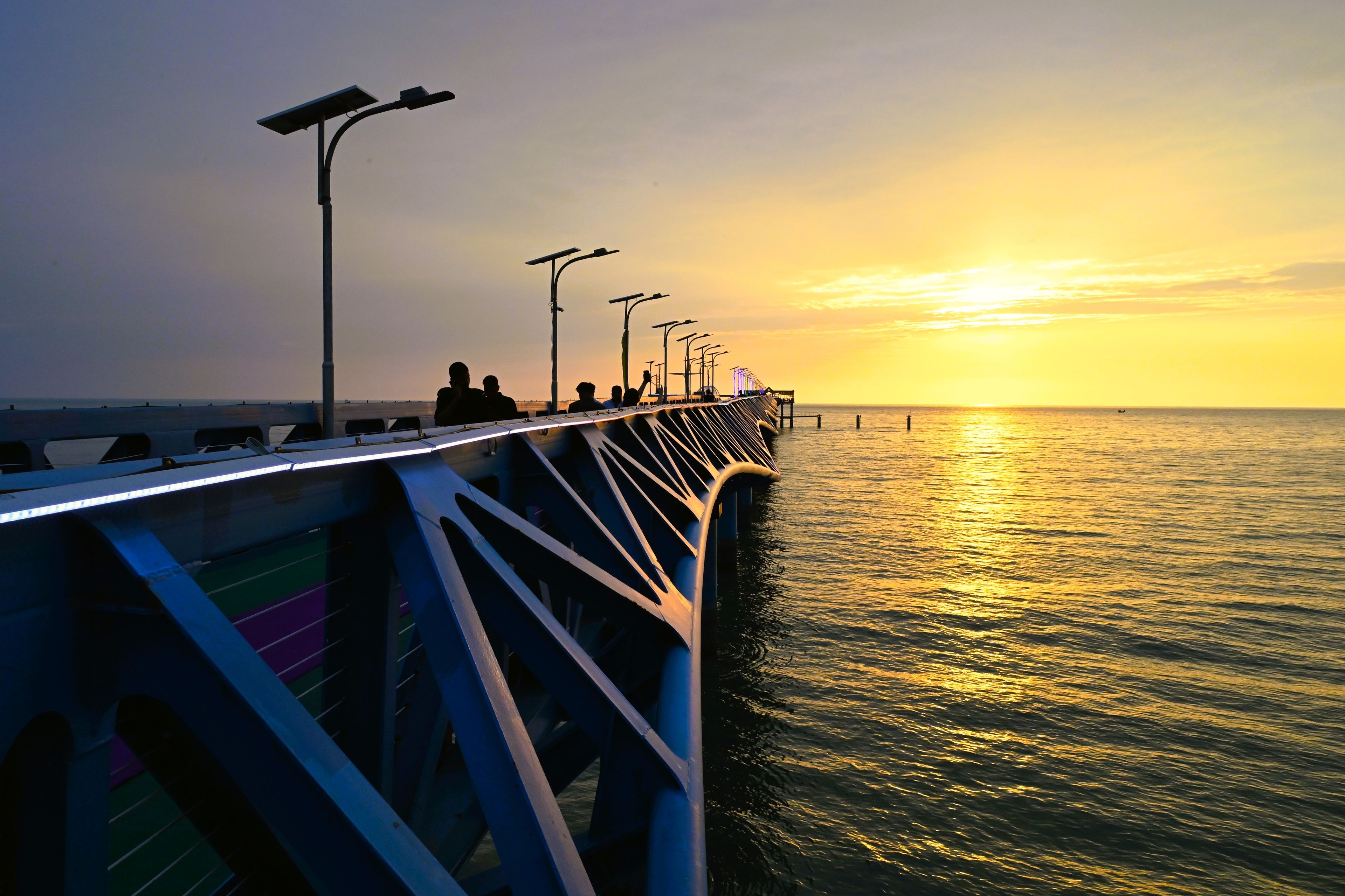 Cox's Bazar District, Chittagong Division, Bangladesh - 14 September 2026: View of the modern metal jetty at Teknaf Beach during a golden sunset, with people walking.