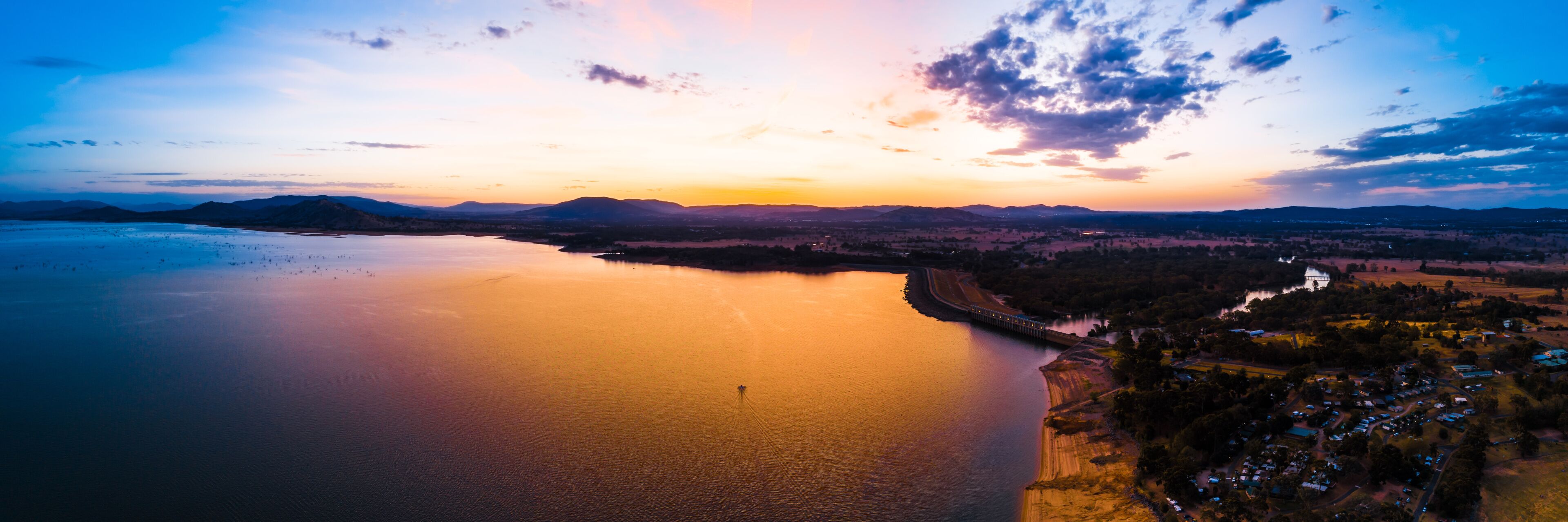 Lonely boat sailing across scenic lake at vivid orange sunset - aerial panorama