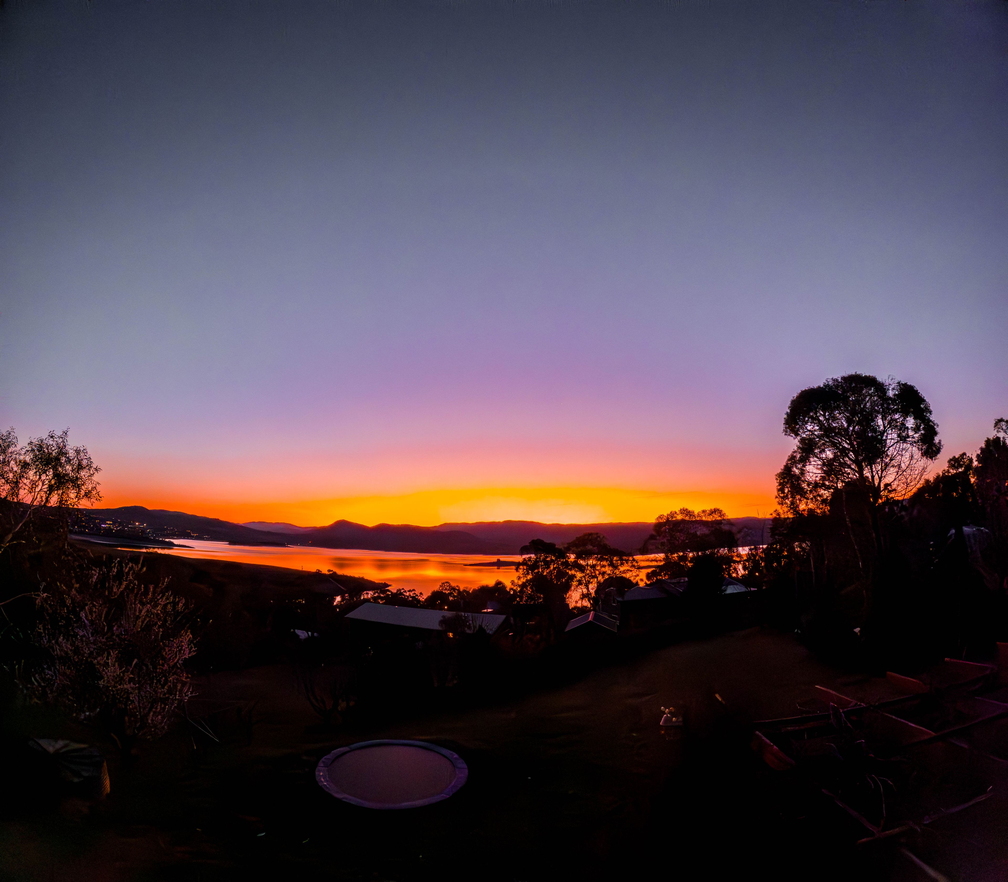 A sunset over a lake with mountains in the background and trees in the foreground.