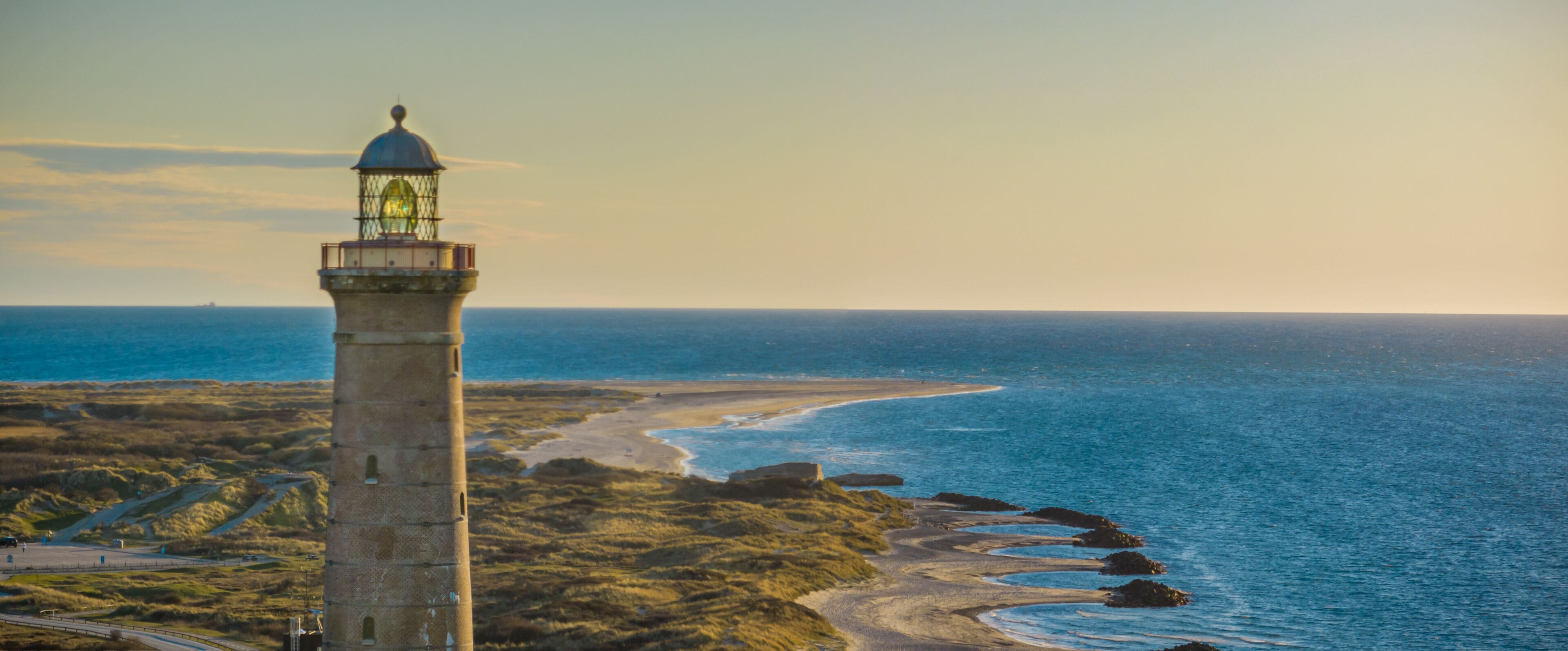 Un paisaje costero con un faro, una playa y una costa rocosa.