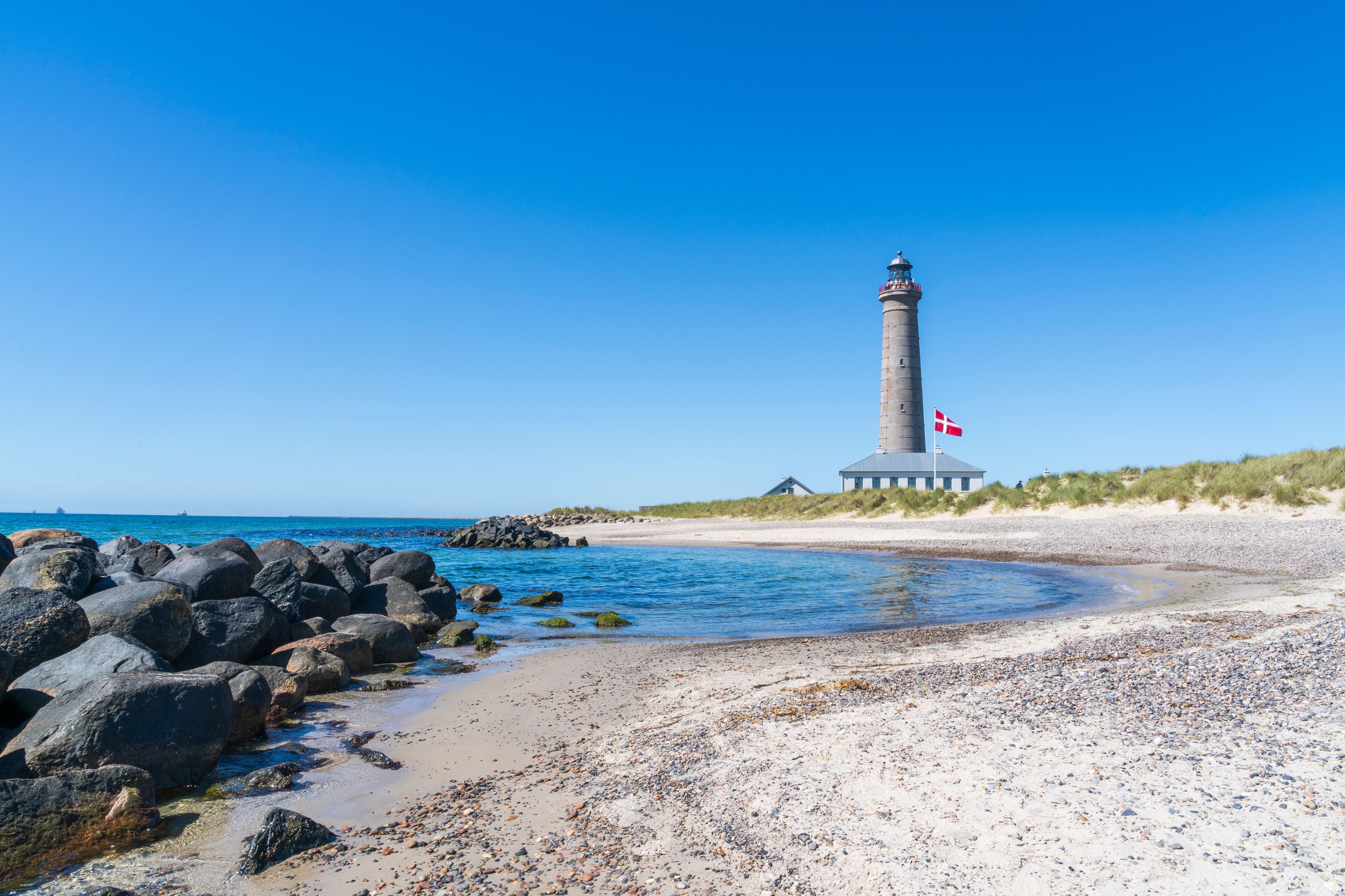 Un faro en una playa bajo un cielo azul despejado.
