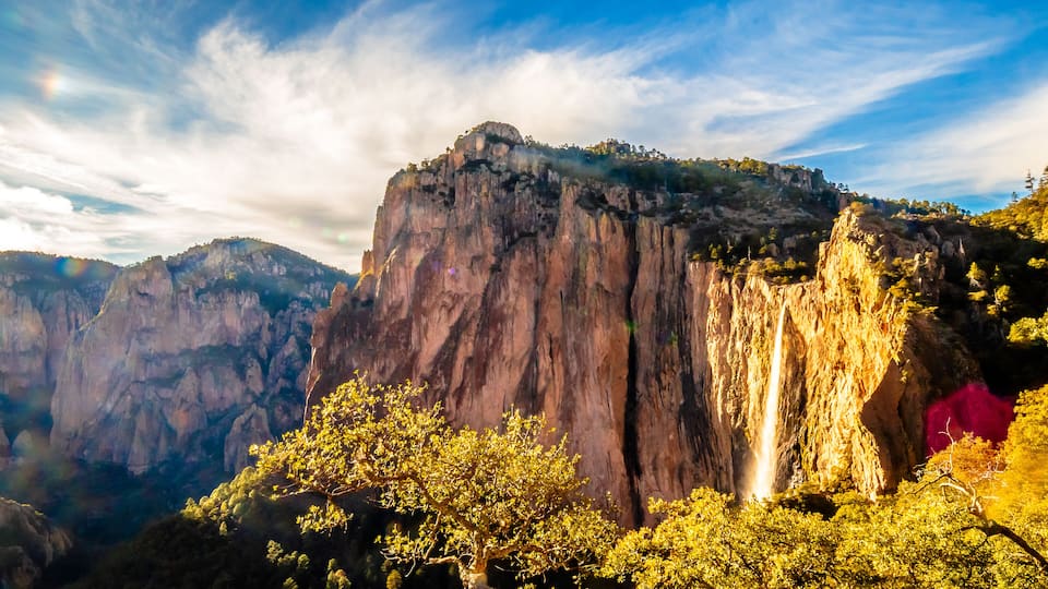 A mountain with a waterfall and dense forest.