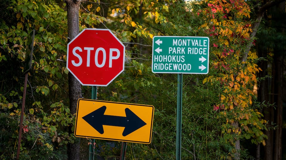 A stop sign, directional signs for Montvale Park Ridge, Hohokus, and Ridgewood, and a two-way arrow sign.