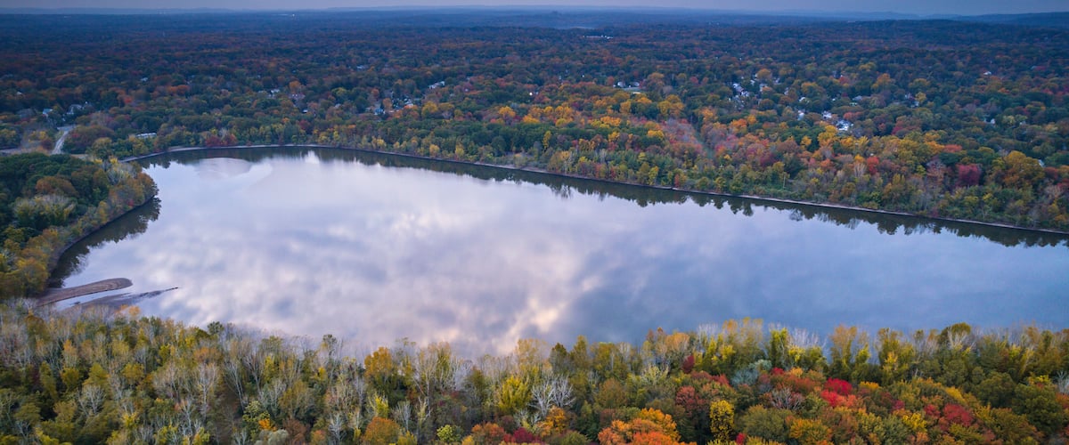 A lake surrounded by autumn-colored trees, a bridge, and a distant town.