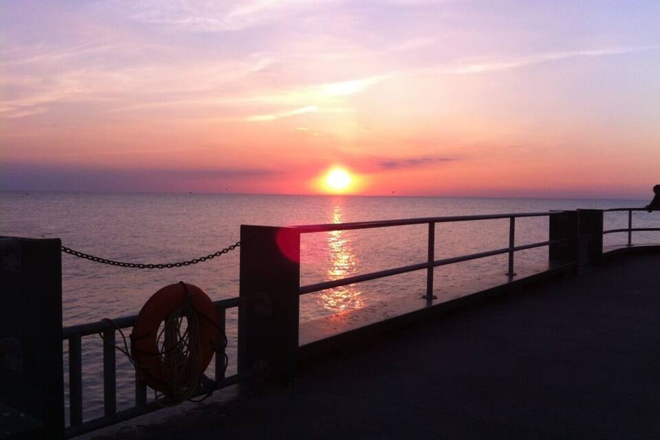 A sunset over the ocean with a pier and a lifebuoy on the railing.