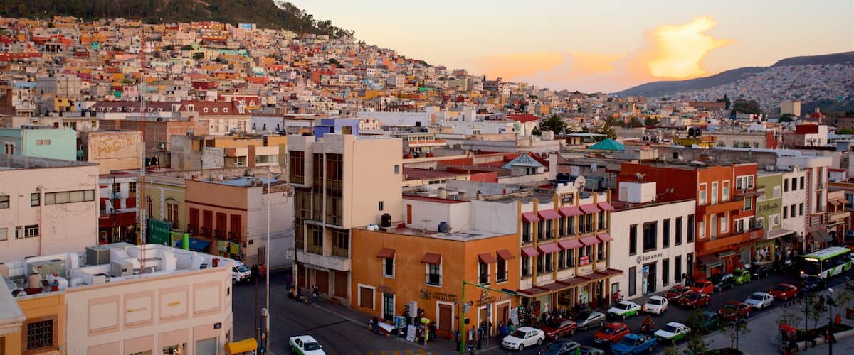 A densely packed urban area with colorful buildings, a prominent hill in the background, and a clear sky.