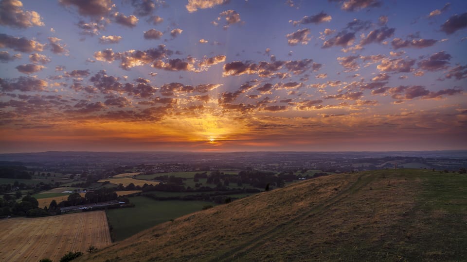 A sunset over a hilly landscape with scattered clouds.