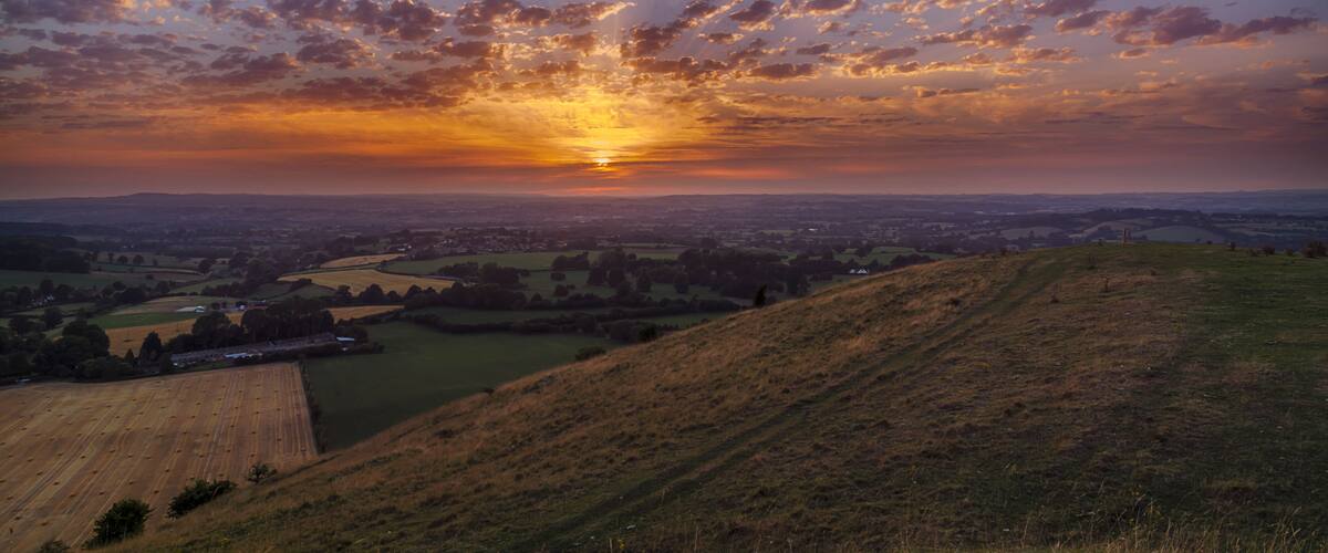 A sunset over a hilly landscape with scattered clouds.