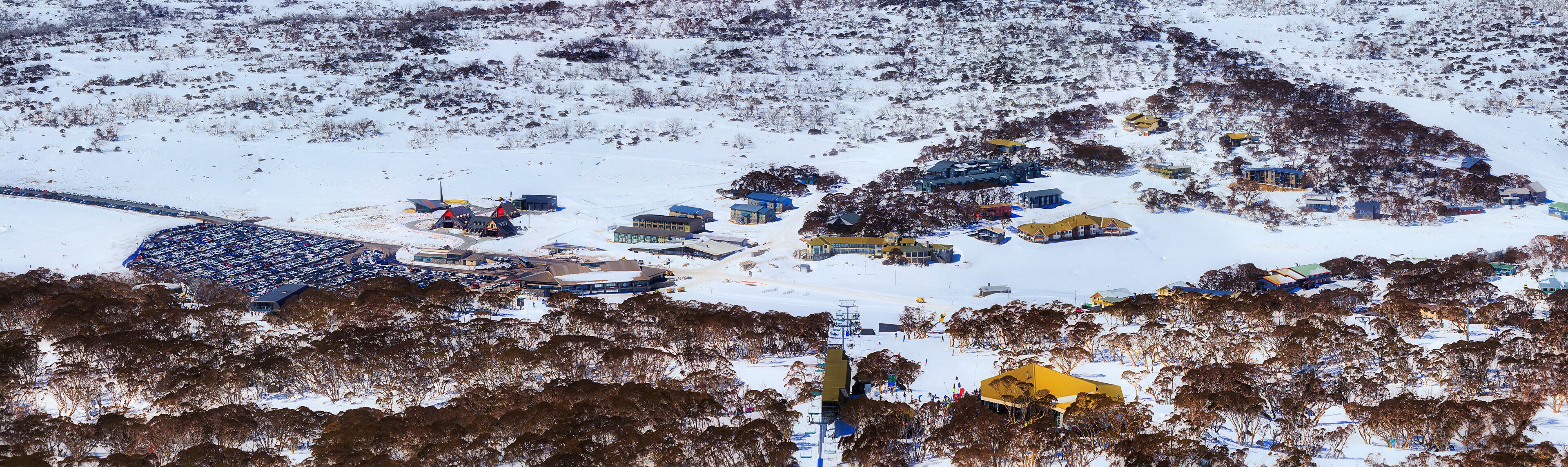 Paisagem coberta de neve com um resort de esqui, edifícios e área de estacionamento.
