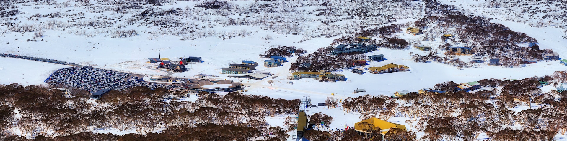 Paisagem coberta de neve com um resort de esqui, edifícios e área de estacionamento.