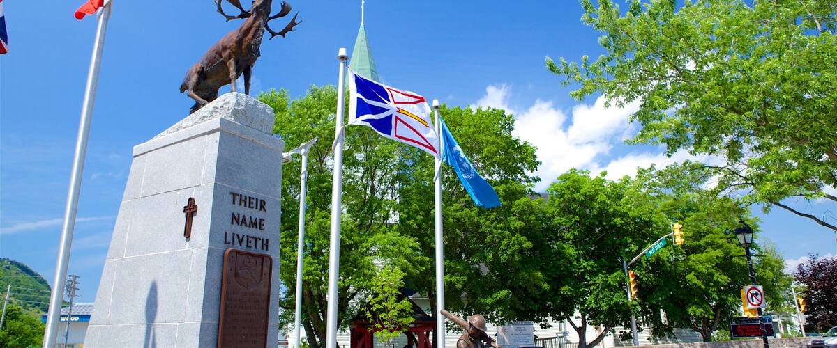A statue of a reindeer on a stone monument with flags and a clear blue sky.