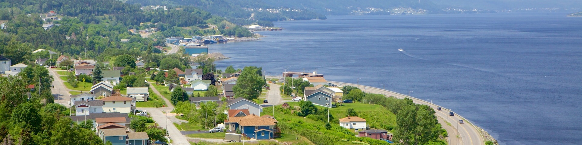 A coastal town with houses along the shoreline, a road curving through the town, and mountains in the background.