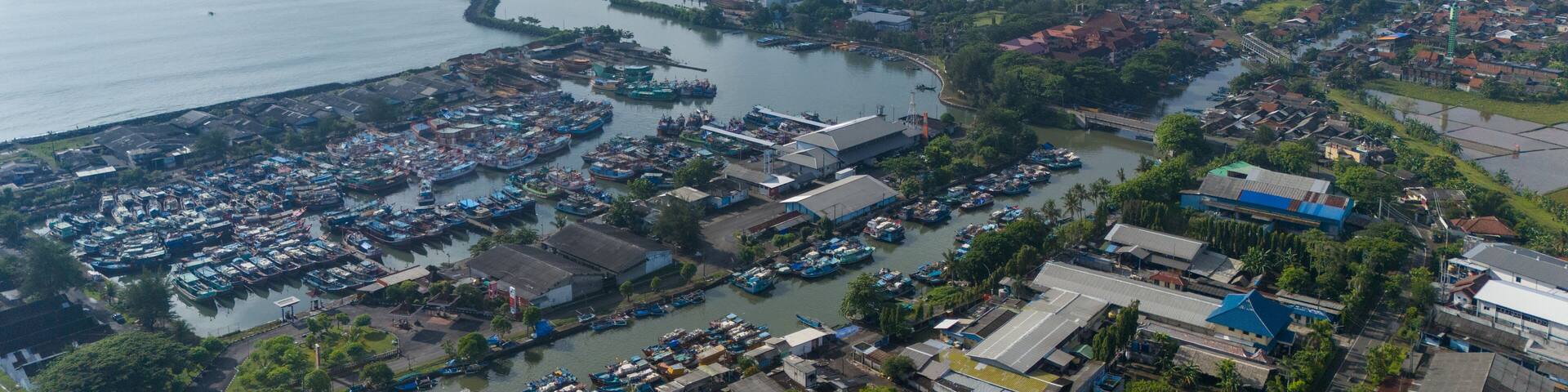 An aerial view of the Cilacap fishing port showcases the Cilacap port and the vibrant coastal cityscape.