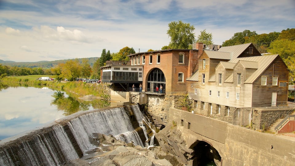 A dam with a waterfall, a river, and buildings with a wooden structure and a brick building.