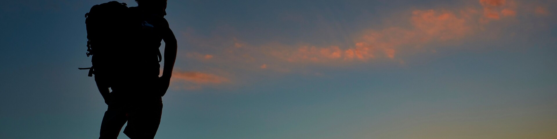 Silueta de una persona caminando con una mochila contra un cielo al atardecer.