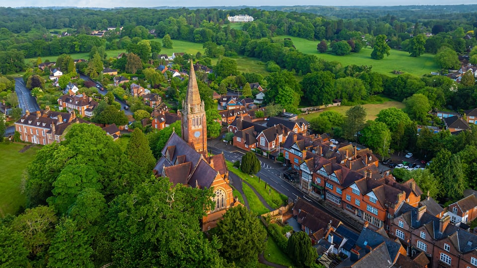 A historic town with a prominent church tower, lush green parks, and a large manor house in the distance.