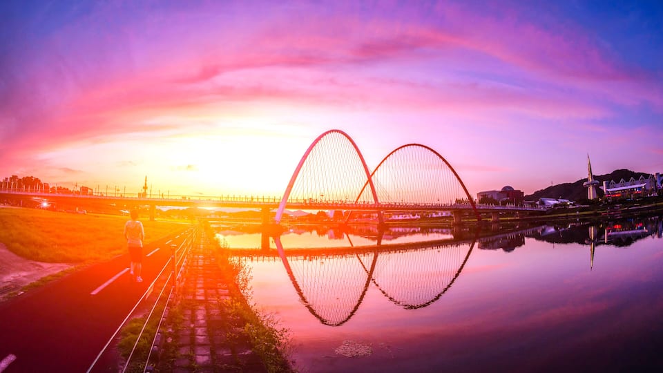 A sunset over a river with a bridge and a distant building.