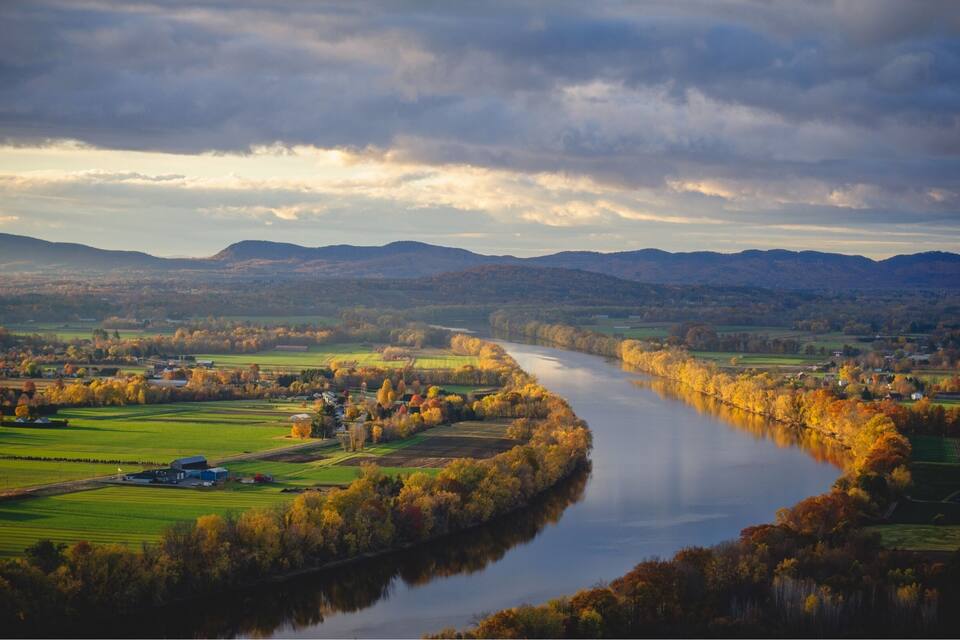 A river winding through a valley with autumn foliage, surrounded by fields and distant hills.