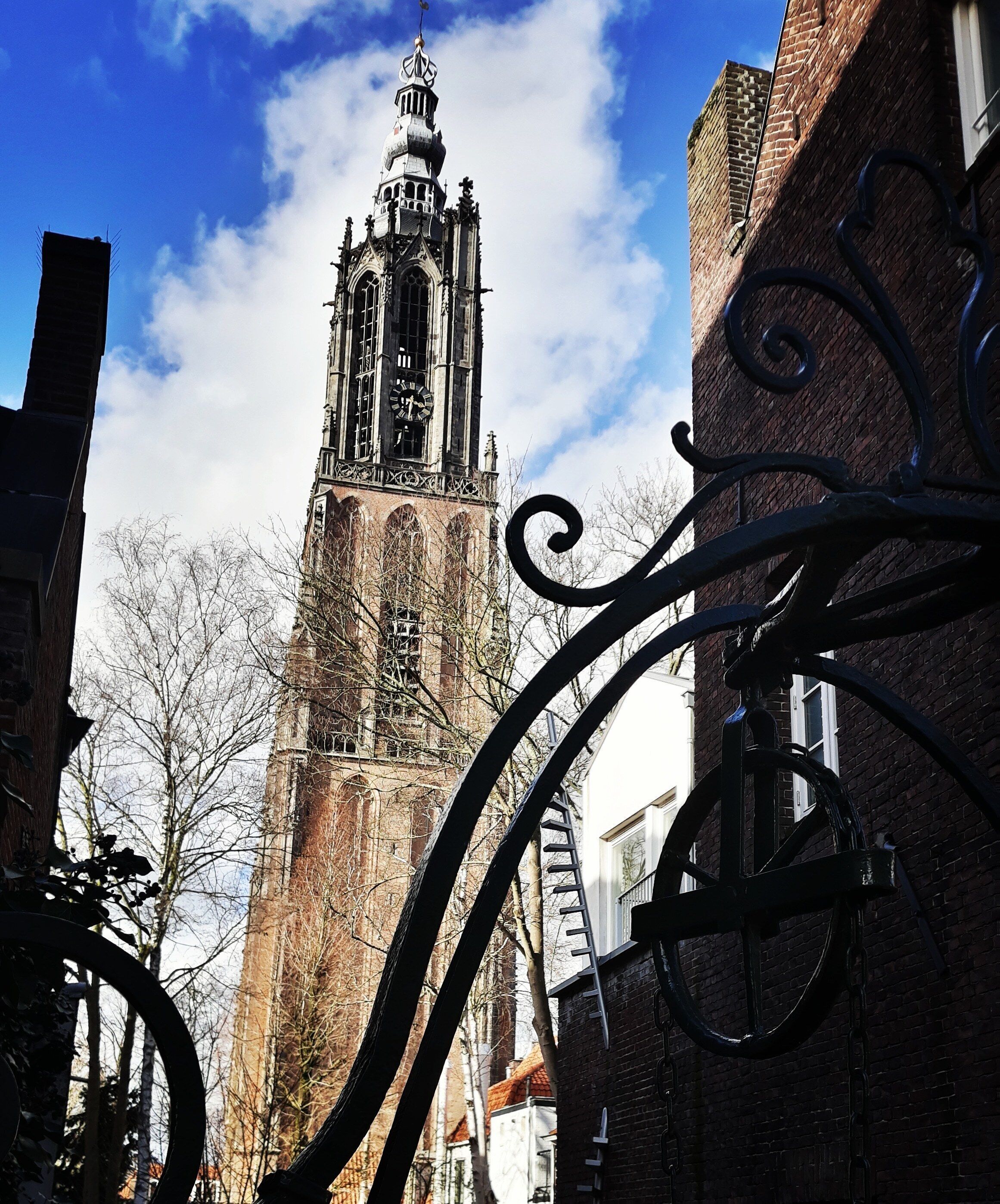 A historic tower with a clock, surrounded by brick buildings and bare trees.