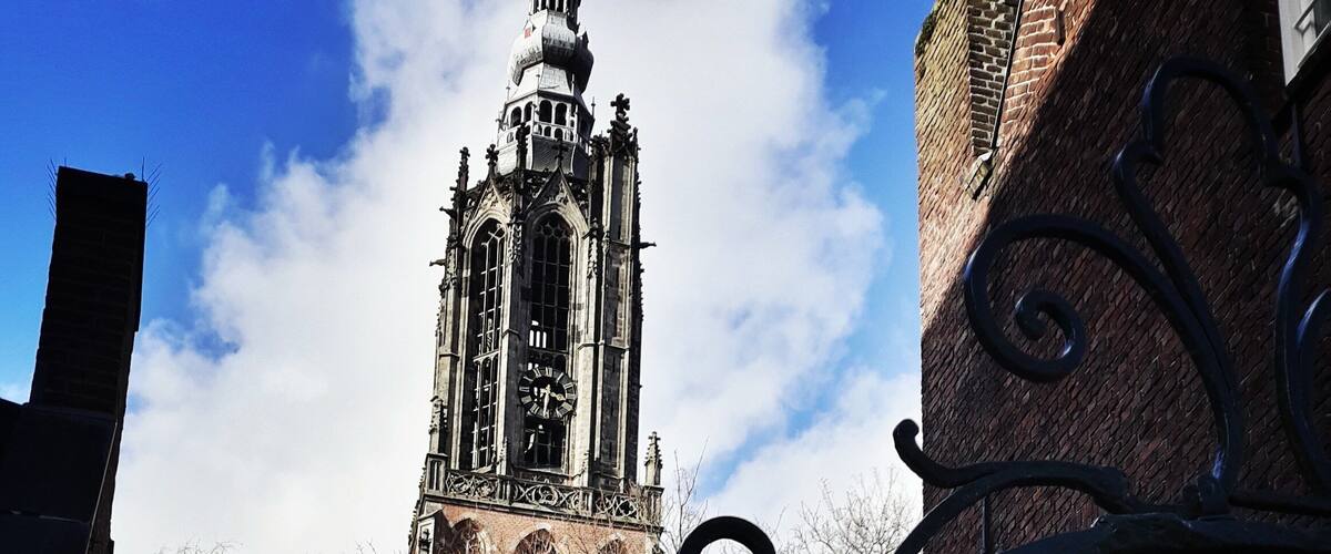 A historic tower with a clock, surrounded by brick buildings and bare trees.
