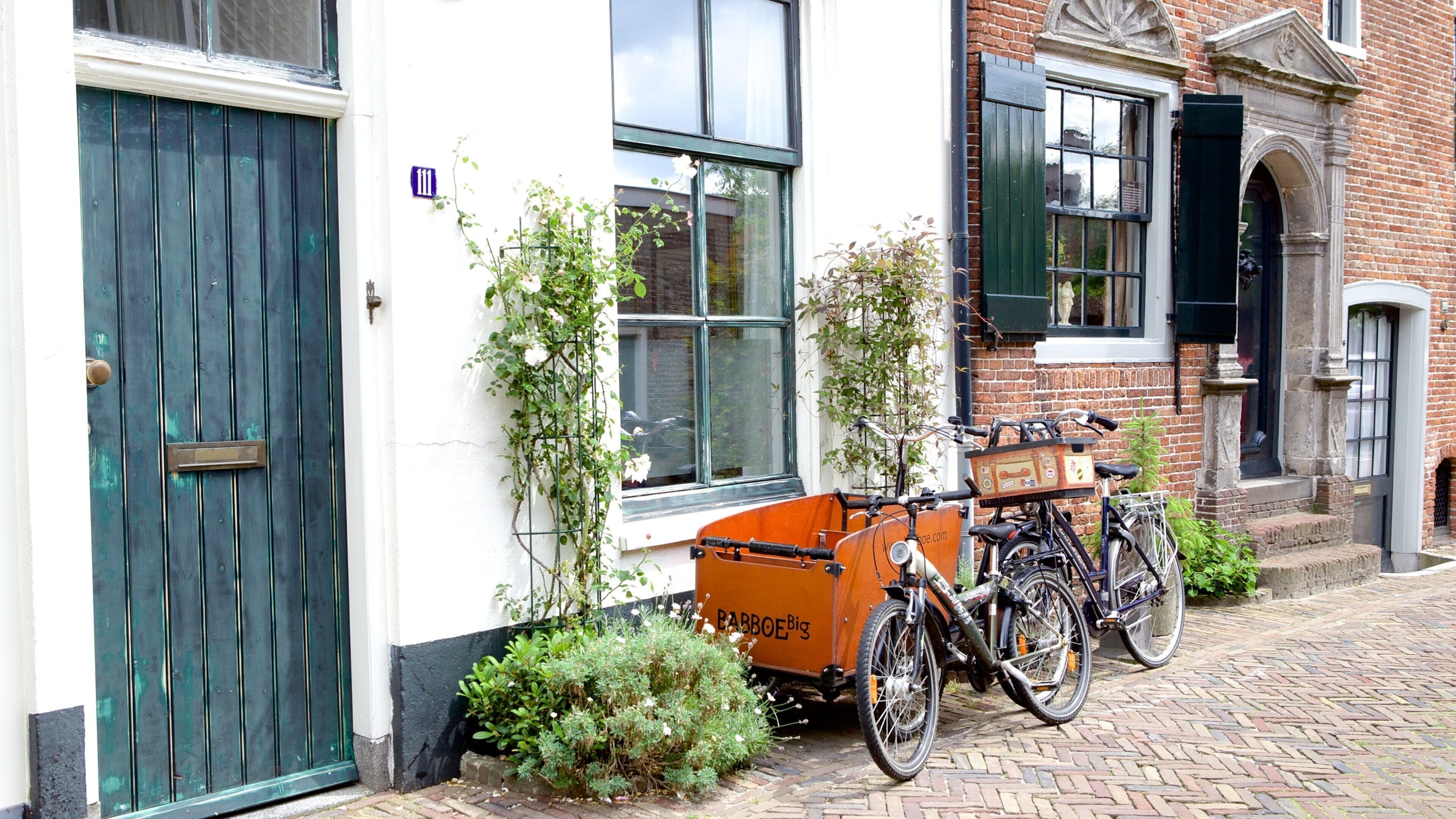 A building with a green door, a window with a white flower box, and a bicycle parked outside.