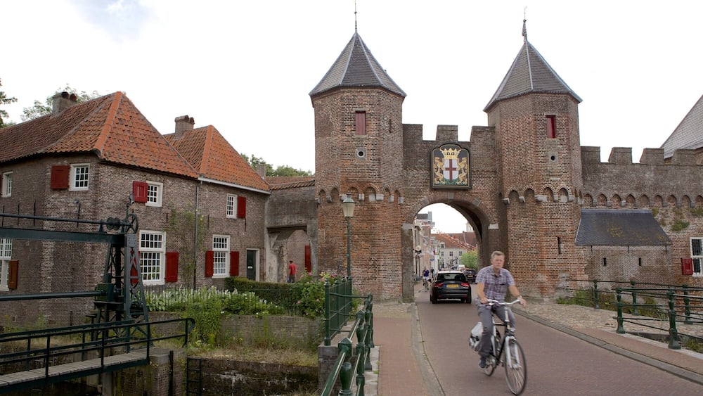 A historic brick gate with two towers, a cyclist, and traditional buildings with red shutters.
