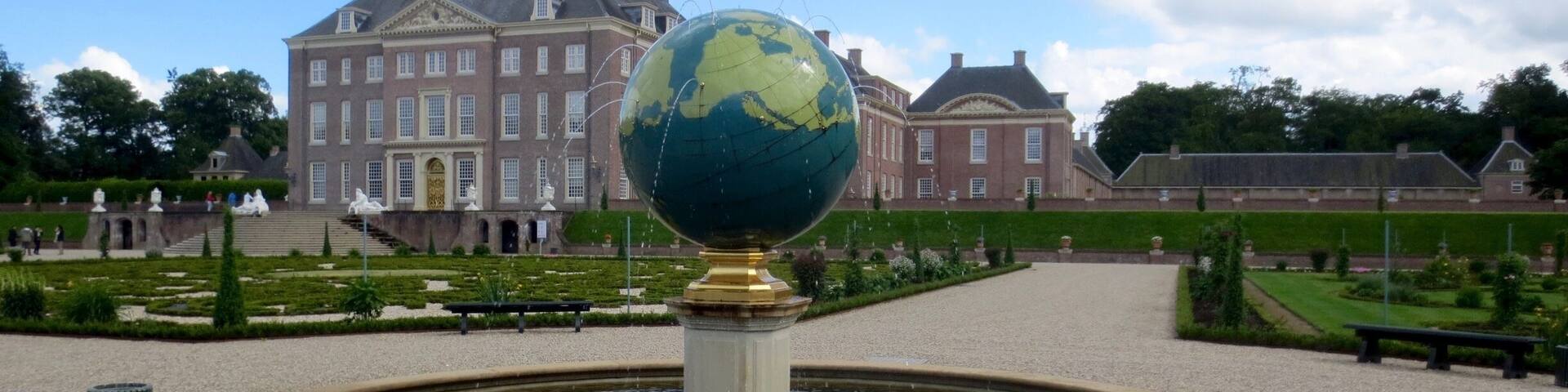 A globe fountain in a formal garden with a large historic building in the background.