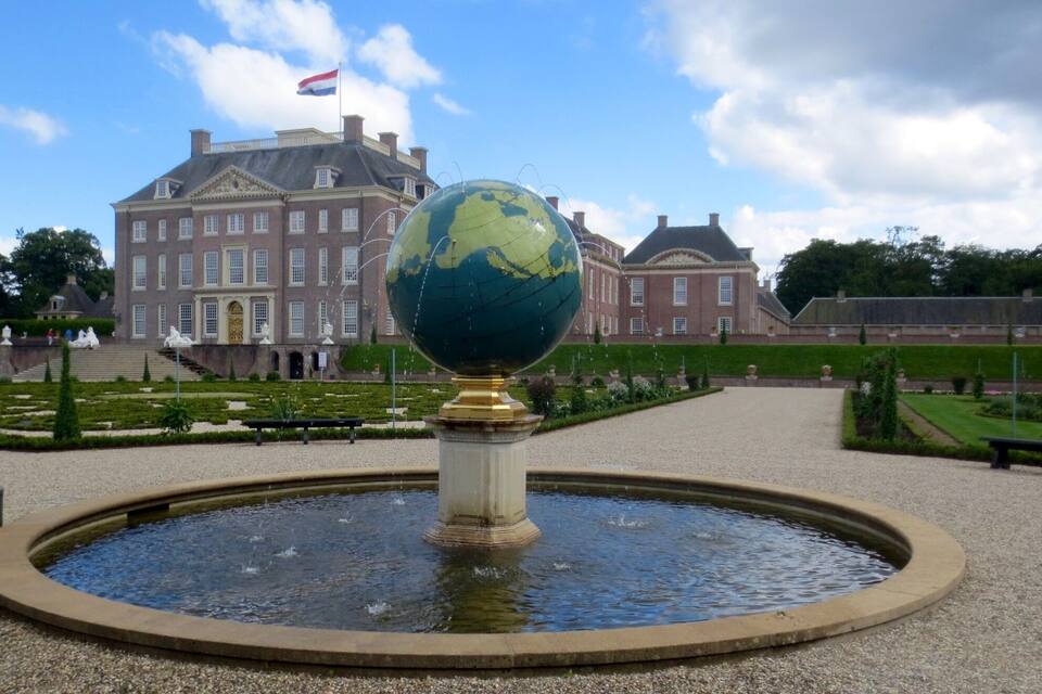 A globe fountain in a formal garden with a large historic building in the background.