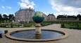 A globe fountain in a formal garden with a large historic building in the background.