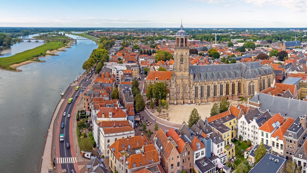 A river flowing through a town with historic buildings and a prominent church with a tall tower.