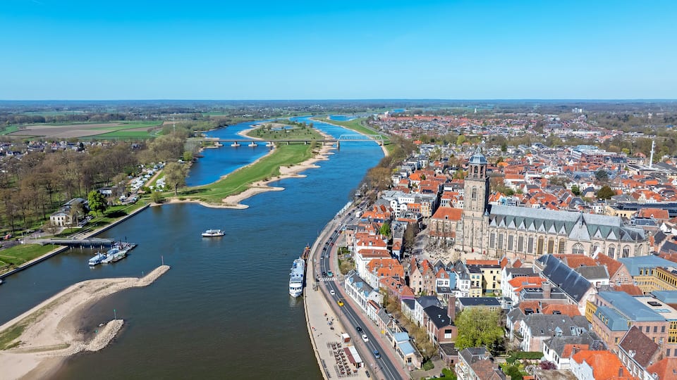A river with boats, a bridge, and a historic town with red-roofed buildings.