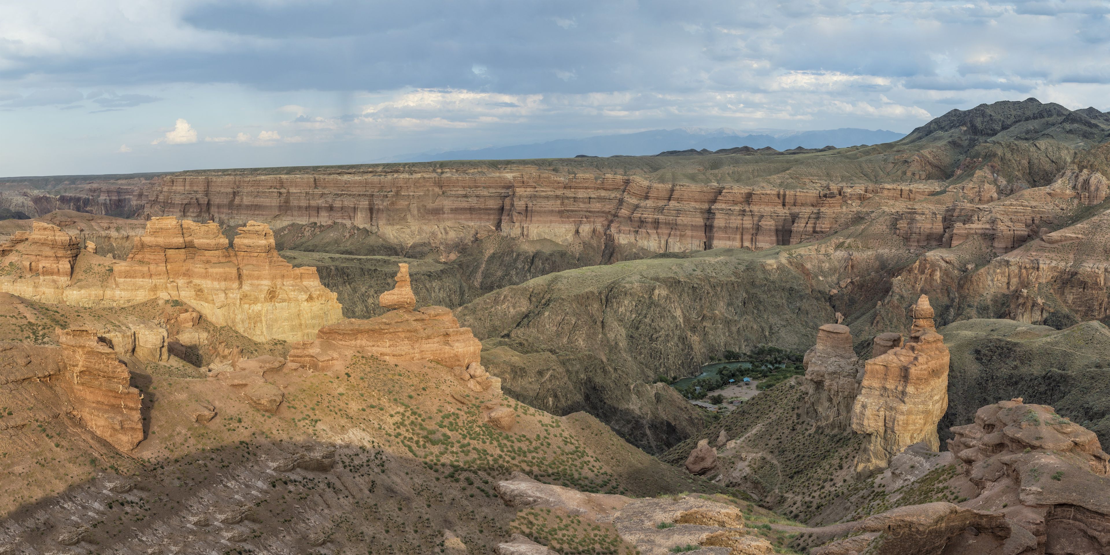 A vast canyon landscape with layered rock formations and sparse vegetation.