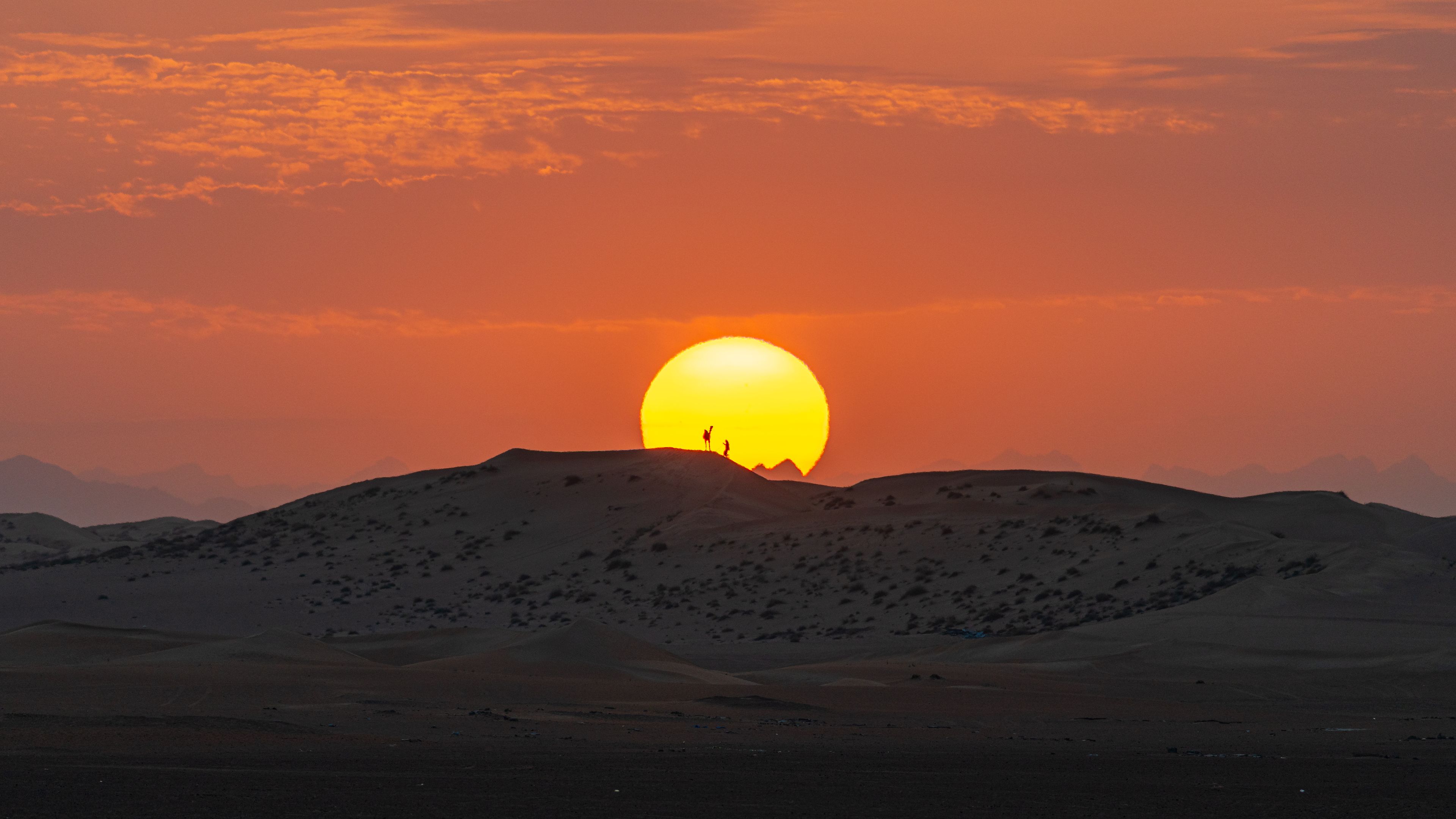 A desert landscape with a large sun setting behind a range of hills.