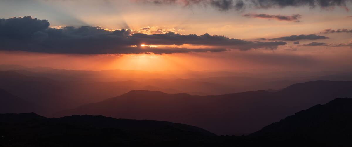 A sunset over a mountain range with clouds.