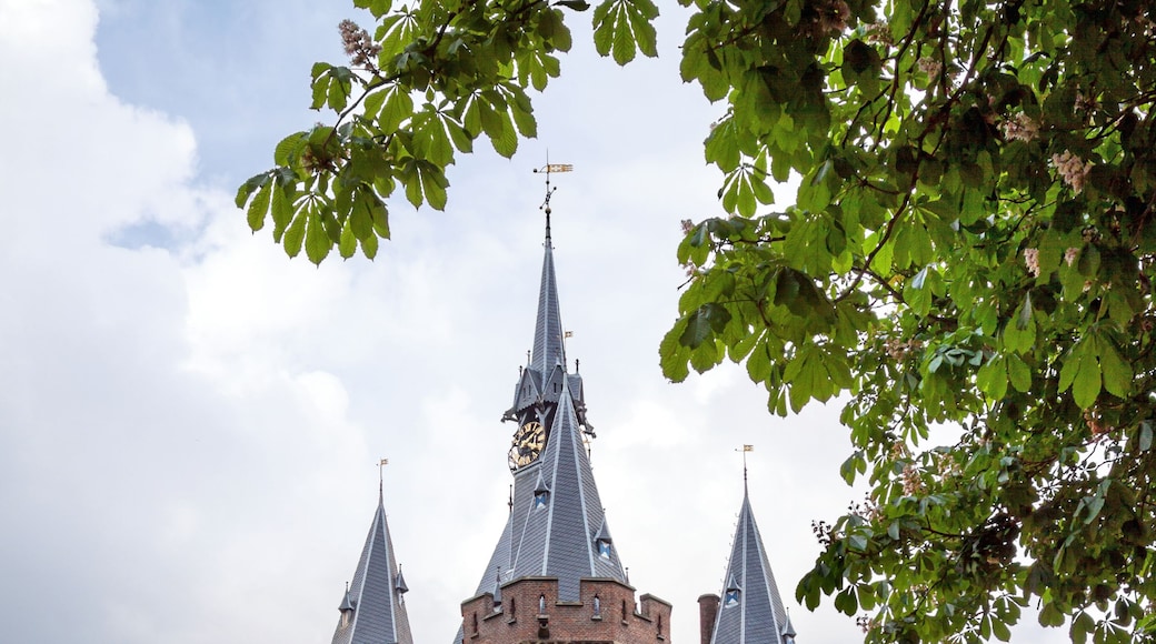 A historic castle with multiple towers and a clock tower, surrounded by modern buildings and pedestrians.
