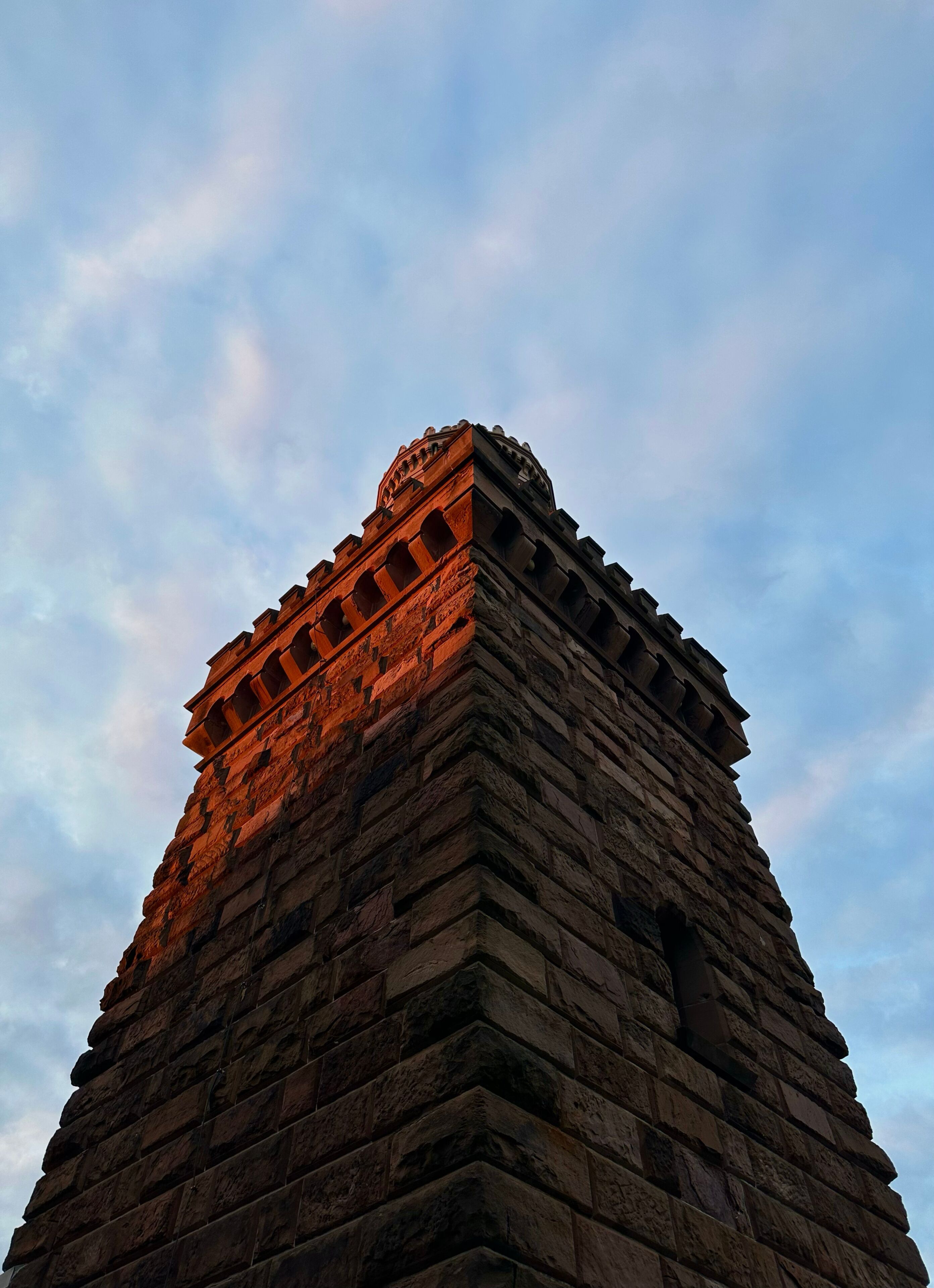 Una torre de piedra con una estructura similar a una pirámide bajo un cielo nublado.
