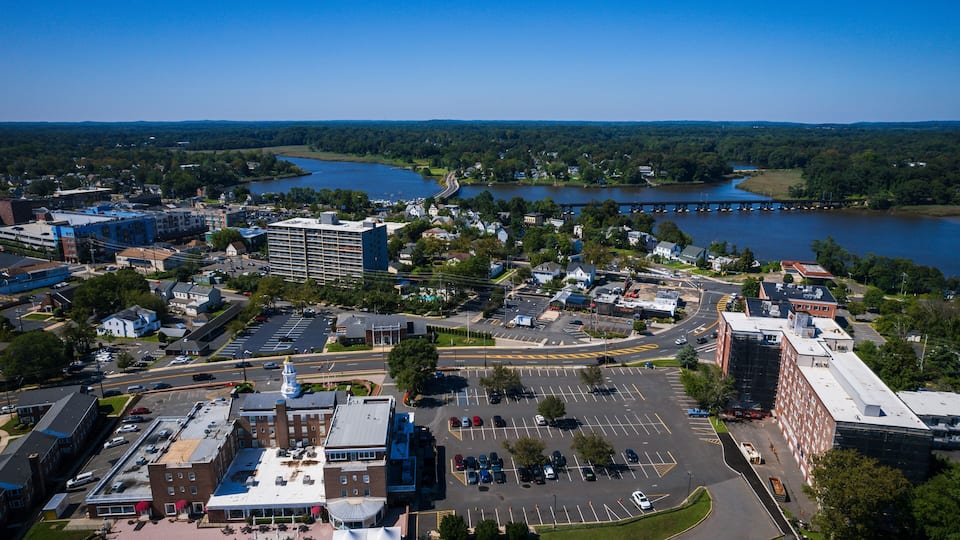 A river with a bridge, a parking lot, and buildings along the riverbank.