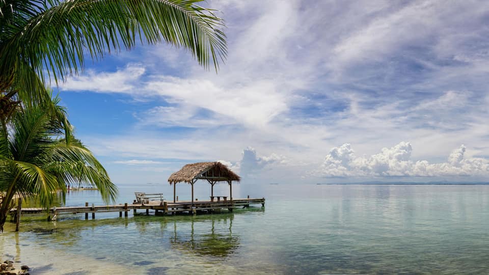 A calm tropical beach with a wooden pier and a thatched-roof hut.
