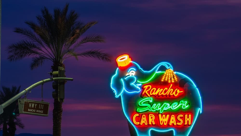 Une enseigne au néon représentant le logo de « Rancho Super Car Wash » sur fond de ciel crépusculaire.