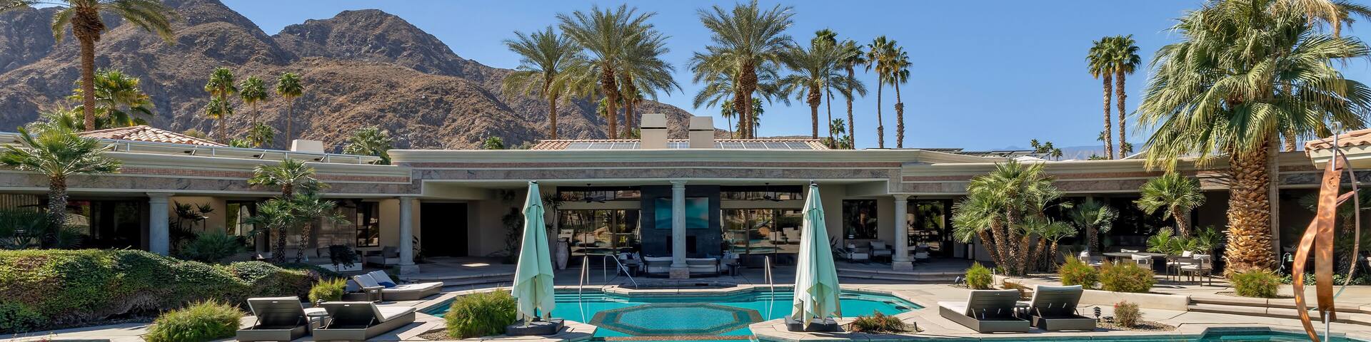 A resort pool with palm trees and mountains in the background.