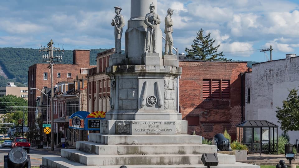 A monument with inscriptions honoring soldiers and sailors from 1861-1865, set in a public square with surrounding buildings and a mountain in the background.