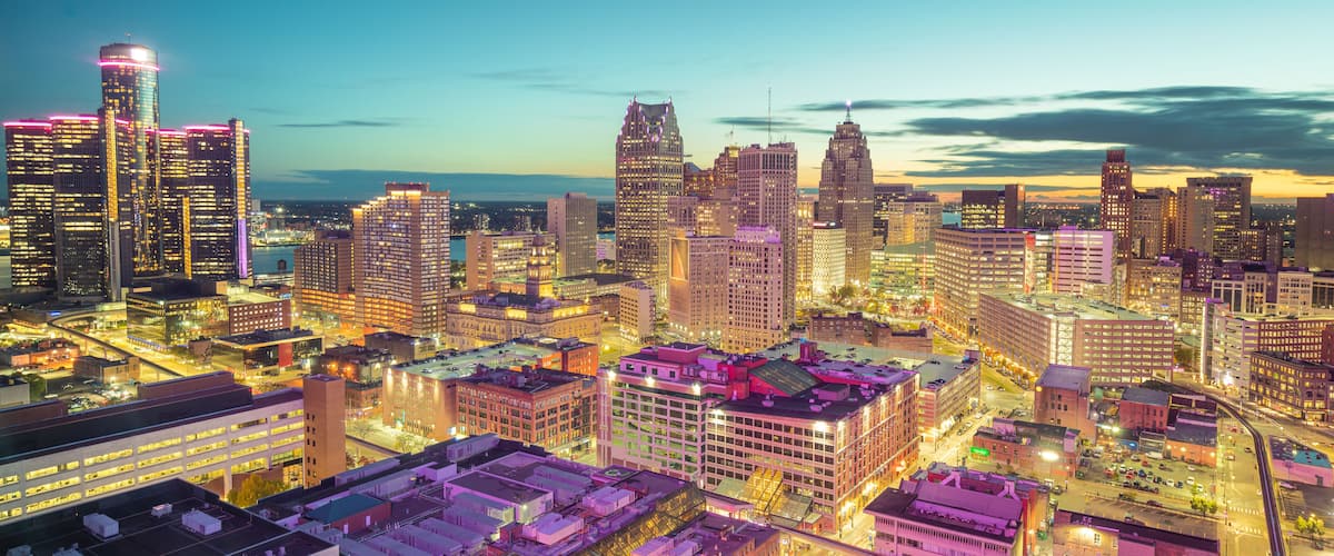 A cityscape at dusk with illuminated buildings and a river in the background.