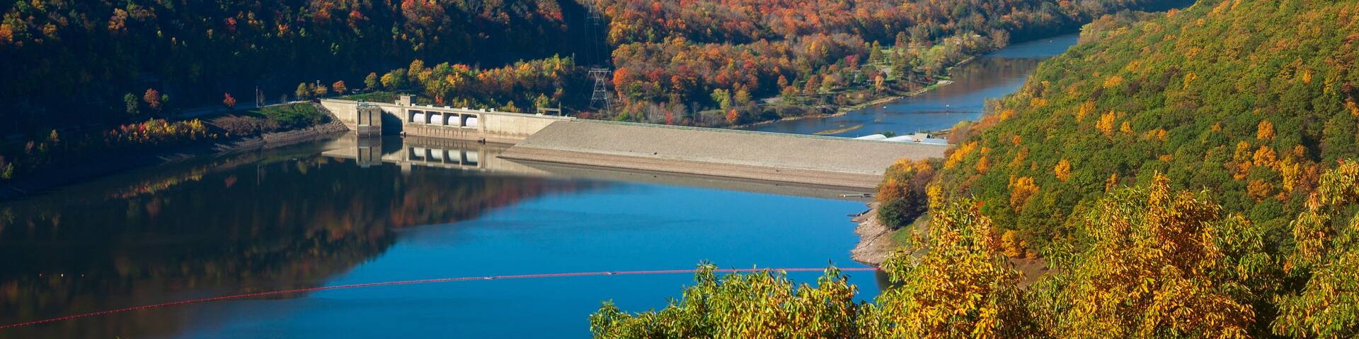 A dam with a bridge, surrounded by autumn-colored trees and a river.
